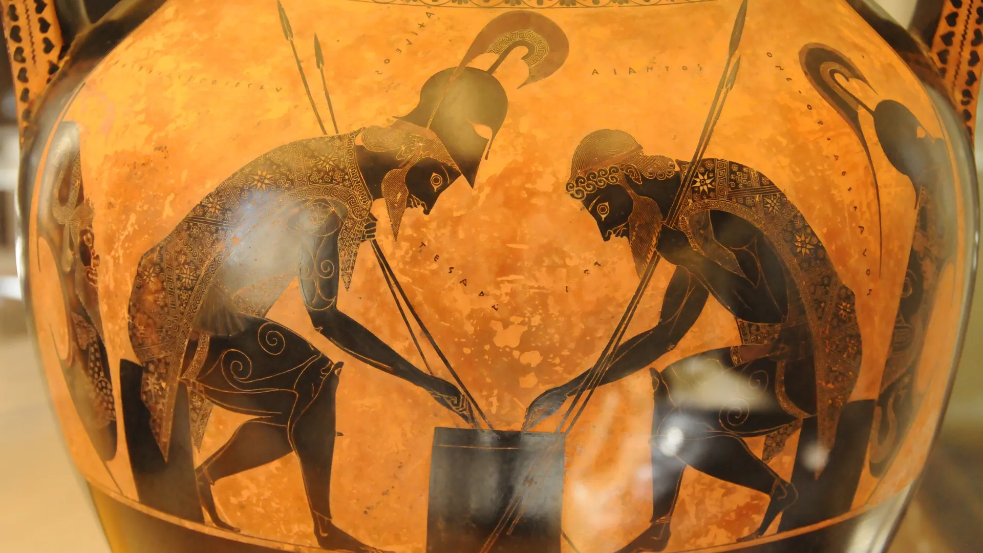 Due guerrieri in armatura sono chini su un gioco raffigurato su un vaso greco arancione, dipinti a figure nere con le lance incrociate tra loro