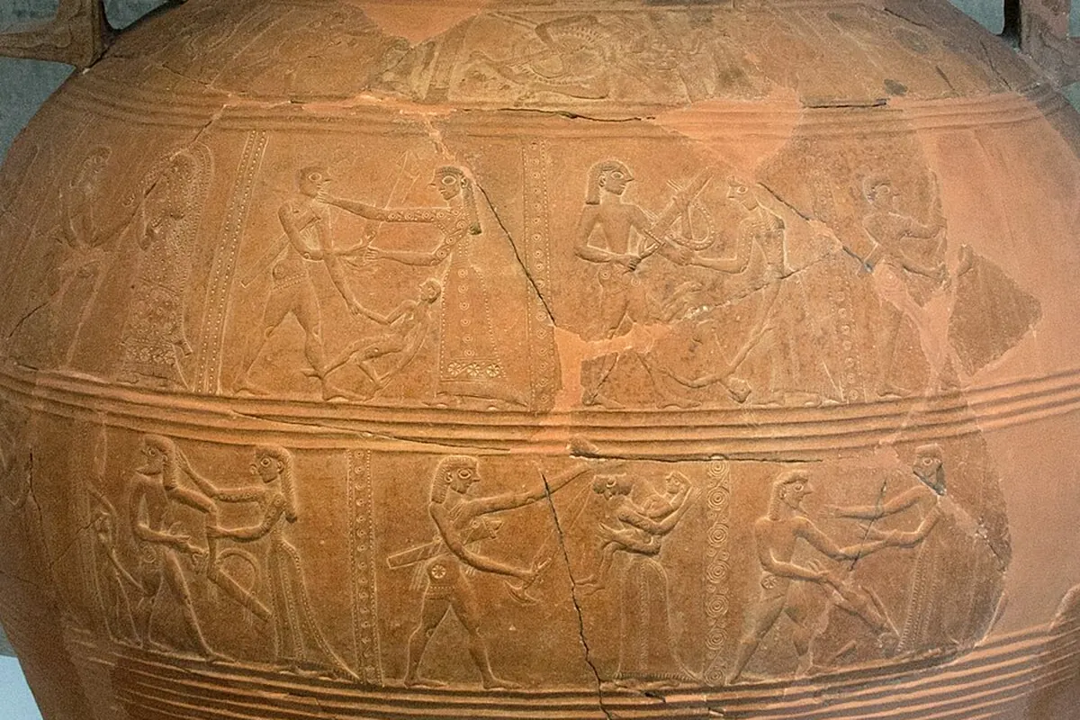 Un grande giara di terracotta per la conservazione, con fasce di figure in rilievo, esposta contro una parete di cemento (il vaso di Mykonos del 675 a.C. circa, che raffigura il sacco di Troia e il cavallo di legno)