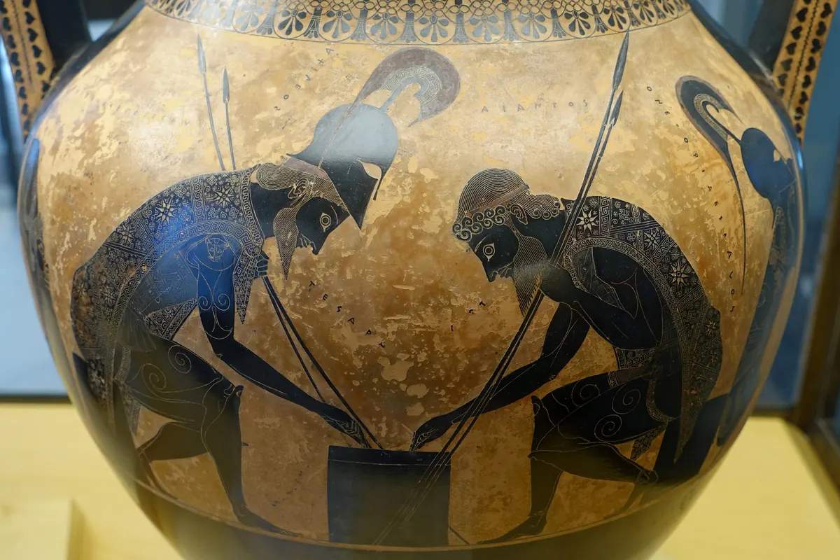 Due guerrieri corazzati chini su un gioco sul pannello arancione di un vaso greco, con una teca museale sullo sfondo (Achille e Aiace su un'anfora attica nei Musei Vaticani, non lo spettacolo)